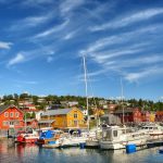 Beautiful and colorful photo of boat houses next to the marina at Hemnesberget with boats in the front on a clear summer day.