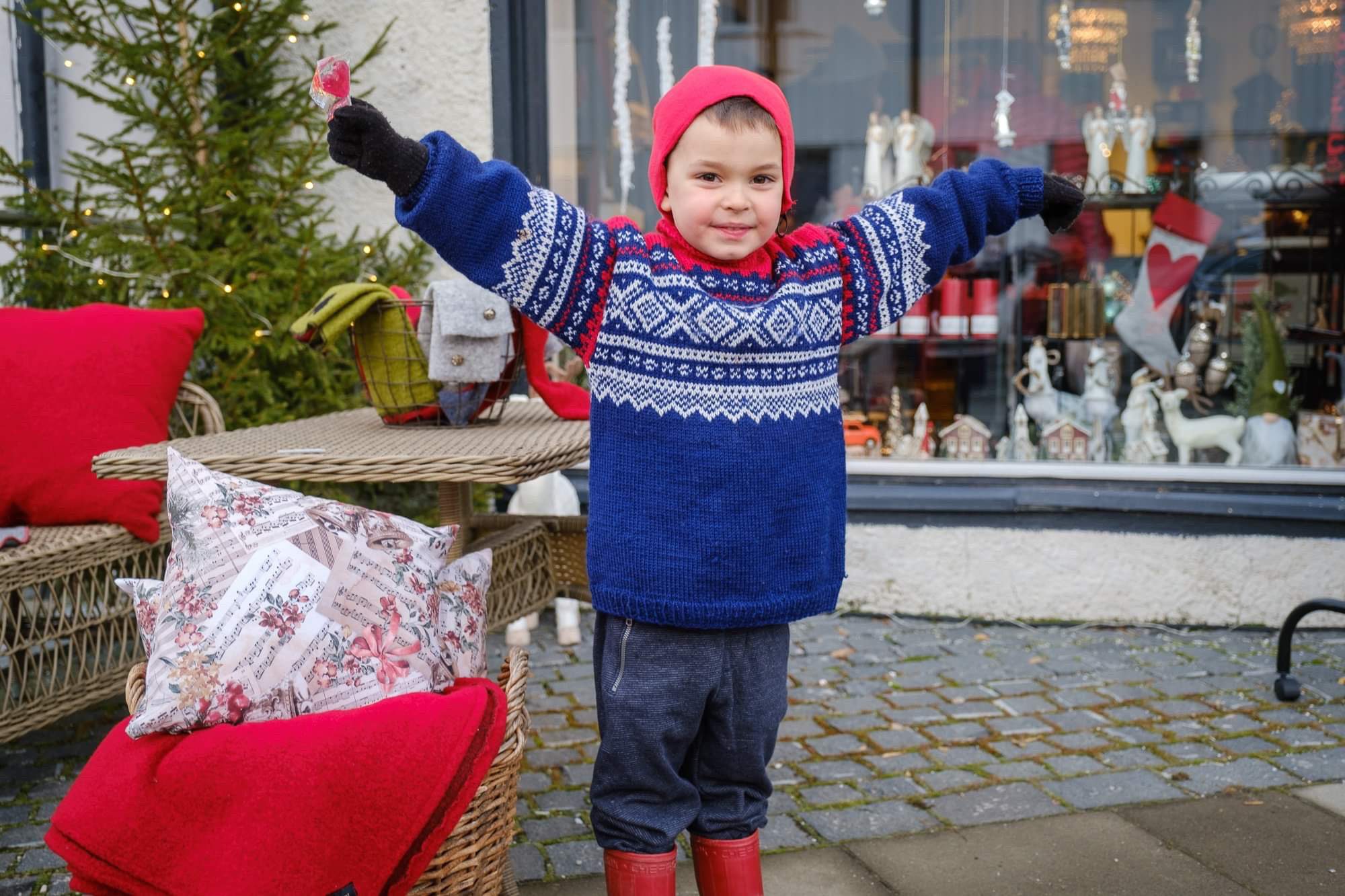 Small boy in norwegian knitted sweater and santa bonnet outside a store