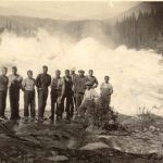 Historic picture of a group of men standing in front of the big and foaming waterfall, Sjøforsen.