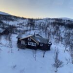 A brown cabin in the mountains with snow on the ground
