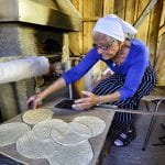 Elderly lady in blue sitting in front of baking oven with “kamkaker” (local pastry) ready to be baked.