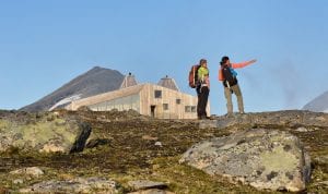 Two colorful hikers standing in front of the designer cabin, Rabothytta, surrounded by magnificent wilderness during summer. 