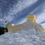 Home-made Easter chicken made from snow with added yellow coloring and a tail of colorful branches as its tail.