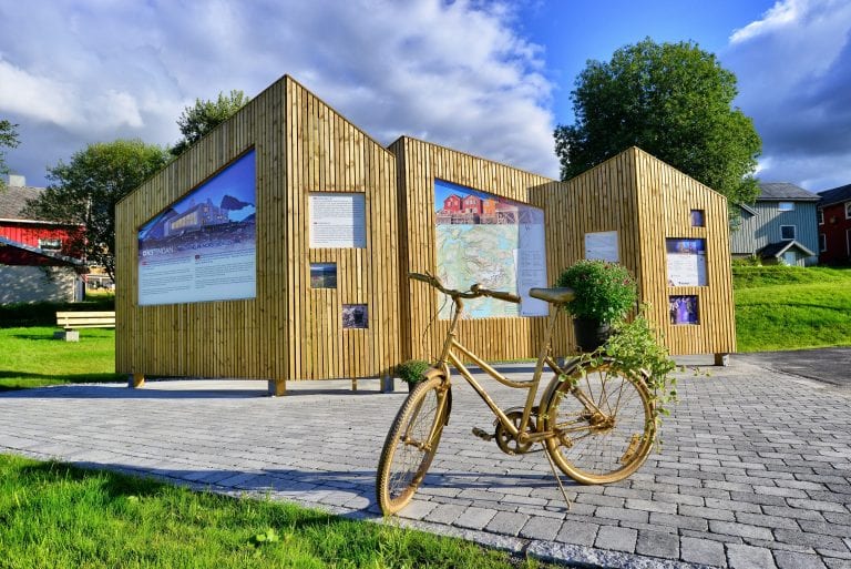 Information board in Korgen made of shining woodwork in the shape of mountains and a matching golden bike in front.