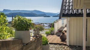 Green plants and decorative stones in front of the entrance of a white house, with a nice view over the fjord and mountains.