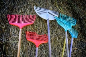 Colorful rakes in blue, purple and red, standing up to a wall of straws as decoration for the outdoor play, Klemetspelet. 
