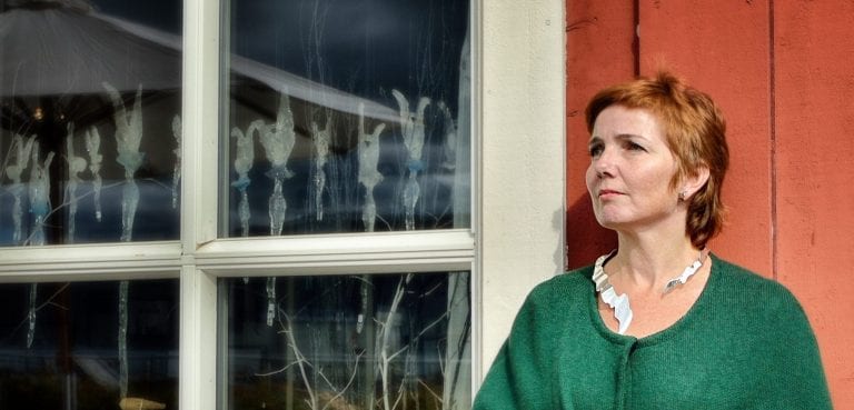 Goldsmith, Merete Mattson, outside in front of her red store with her work hanging in the window and another on her neck.