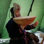 The sami, Frank, in a sami-costume inside a lavvo holding a sami drum.