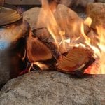 A coffeepot laying on an open, yellow fire that is surrounded by stones.