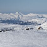 The cabin, Rabothytta, seen from the glacier above, with a view over a chain of snow-covered mountains in the horizon.
