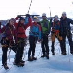 Six happy people equipped with rope, crampons and ice axe on a glacier.