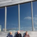 Three happy men sitting in front the cabin, Rabothytta, and its panorama windows while enjoying the summer sun.