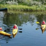 Several kids kayaking in yellow kayaks and red life vests, in Bleikvasslia during a mountain camp arranged for children.