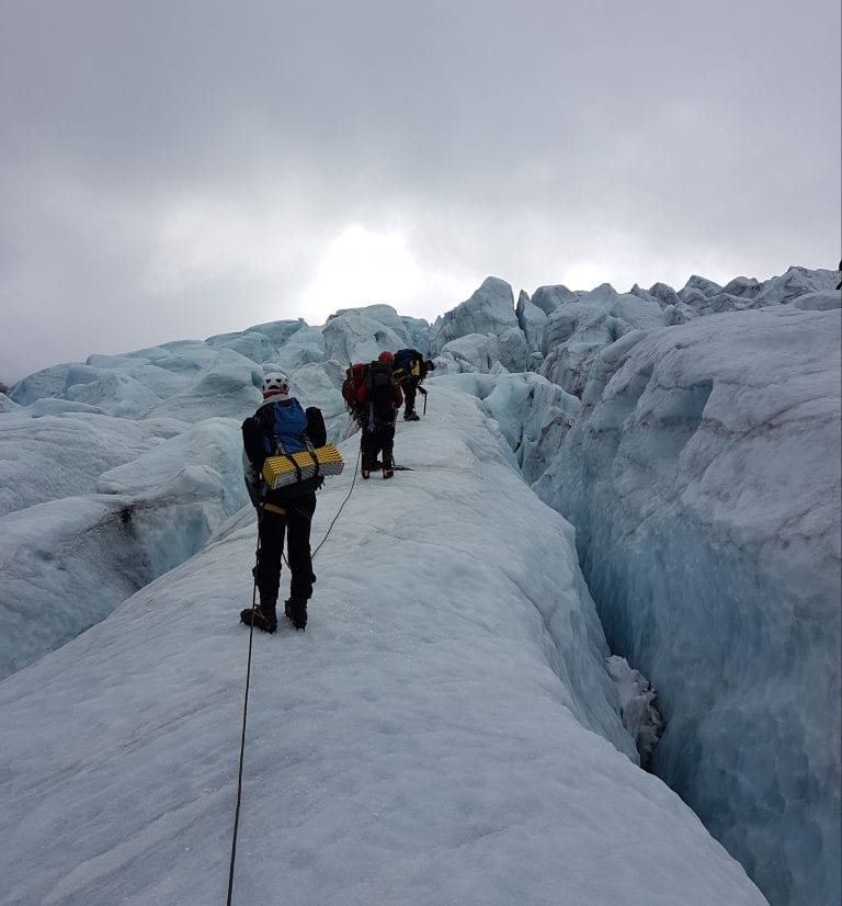 People climbing a steep glacier filled with crevasses, together with ropes between each other.