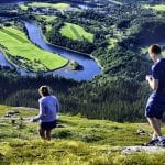 Two people walking down a green mountain with a view over the forest and the river, Røssåga, in a U-formation.