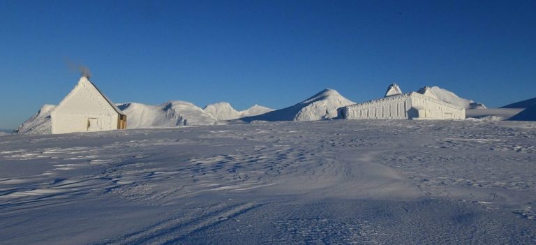 Rabothytta and Klemetstua covered by snow with white mountaintops in Okstindan in the background.