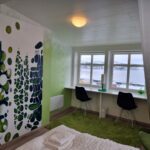 A green room with two windows and a big painting on the wall.