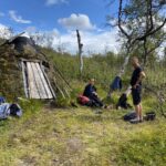 Two hikers in front of a traditional hut.