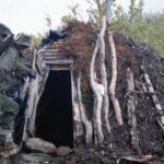 A hiker with a big backpack standing outside a traditional sami hut, looking in.