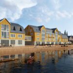 Two big yellow wooden buildings on the fjord with people and a kayak in front