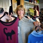 Anne-Lise, the owner of “Kråkeslottet” smiling and standing inside her store holding some of her colorful clothing products.