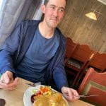 A smiling man in front of a plate with salad, meat and sauce.