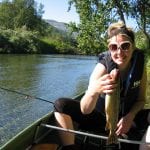 Happy woman holding a self-caught fish in the sun, while sitting in a rowboat on the lake next to Stekvasselv Farm.