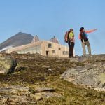 Two colorful hikers standing in front of the designer cabin, Rabothytta, surrounded by magnificent wilderness during summer.
