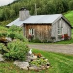 The small and old cooking house at Inderdalen Farm surrounded by green grass and people drinking coffee outside it.