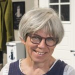 Portrait of Anne-Lise from Kråkeslottet in a dress designed and made by herself, standing in front of her shop.