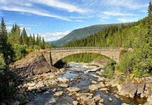 The bridge over the waterfall, Sjøforsen, with green nature surrounding the waterfall and the mountain, Klubben, in the back.