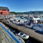 The marina with boats and people enjoying the sunny day from the boat or from outside the red café next to the marina.