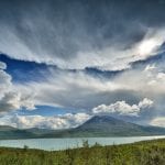 The lake, Røssvatnet with mountains in the horizon behind it, and a powerful cloud-filled sky.