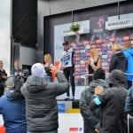 The winner of the Artic Race standing on stage at Korgfjellet with a bouquet up in the air and the press taking pictures.