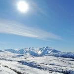 White mountains during a sunny winter day with a view over the mountain, Lukttinden, in the horizon.
