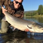 Happy fisherman standing in the river, Røssåga, with the water to his knees, holding a huge salmon he has caught.