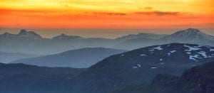Layers of mountains as long as the eye can see under a burning orange/yellow sky, seen from Rabothytta.