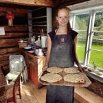 Smiling young lady holding a tray of freshy made “kamkake”, local bread, standing inside the old and wooden baking house.