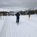 Skier in the scooter track, standing by a speed sign, on a cloudy winter day.