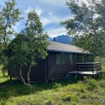A brown cabin surrounded by birch trees and mount Oksskolten in the background