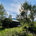 The cabin Gressvasshytta with mountains in the background and green trees in the front.