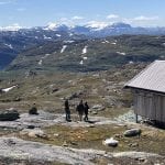Hikers walking towards the cabin, Gråfjellhytta, during summer with a view over a big lake and more mountains in the horizon.