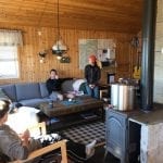 People sitting in a cozy living-room inside a cabin in the mountains with the sun shining in through the windows.