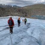 People walking with rope and crampons next to a huge crack in the glacier.