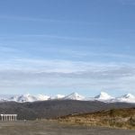 Info board in front of a panoramic view over several white mountain tops in Okstindan