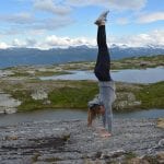 Girl doing a handstand on a rocky peak in front of small lakes with the Okstindan-mountains in the background.