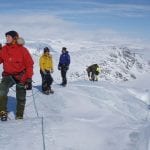 Colorful people walking with ropes between them up the glacier in Okstindan, in completely white winter surroundings.