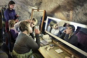 Young girls in old costumes putting on make-up in front of a mirror, preparing themselves for the local play, Klemetspelet.