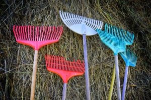 Colorful rakes in blue, purple and red, standing up to a wall of straws as decoration for the outdoor play, Klemetspelet.