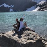 Two happy girls sitting on a rock in front of the shining glacier-lake close to Rabothytta on a sunny summer day.